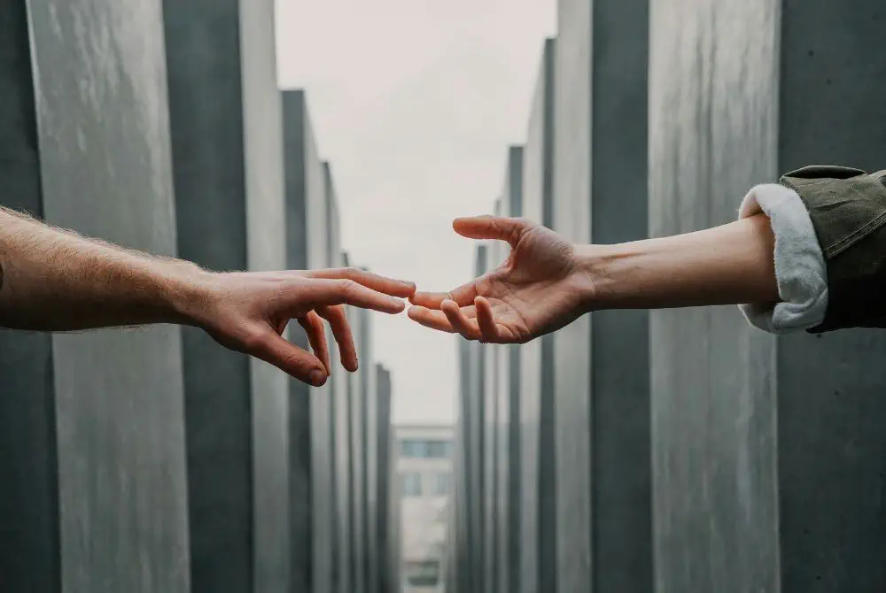 Two hands reaching toward each other between concrete pillars