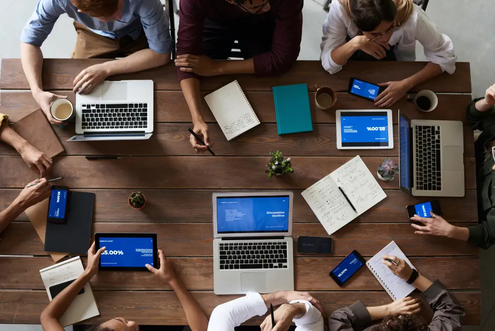 Overhead view of a team working on laptops, tablets and phones at a wooden table