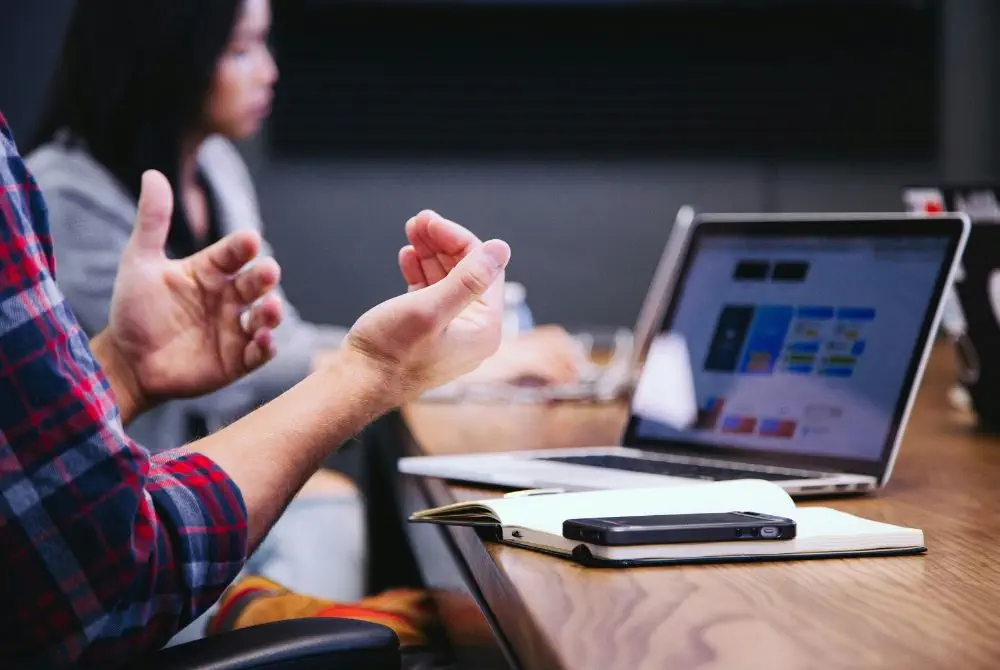 Person gesturing during a discussion beside an open laptop