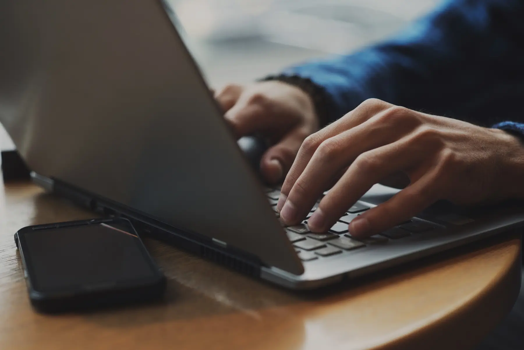 Hands typing on a laptop with a phone on the desk